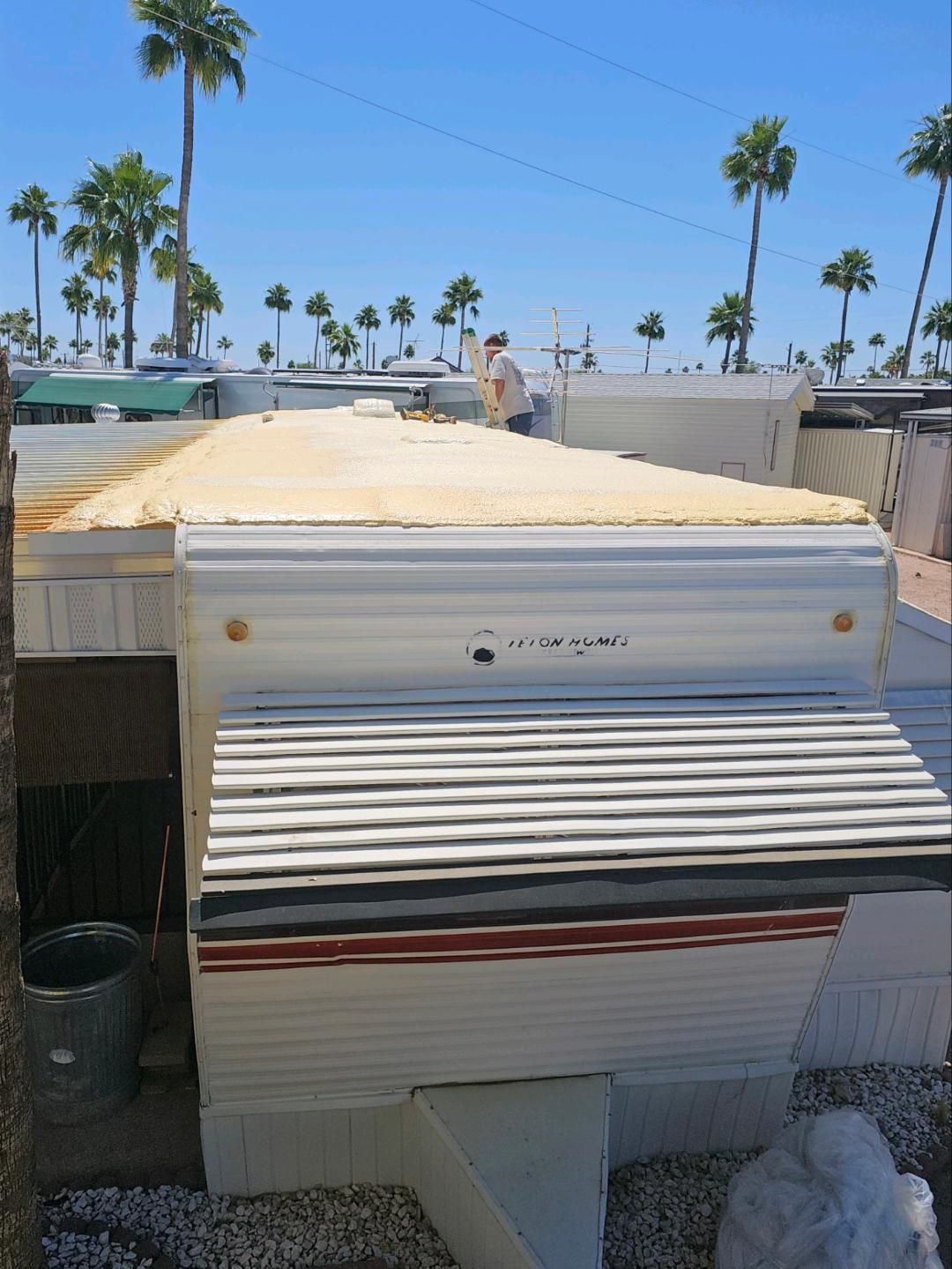 White rooftop unit with a striped awning under a sunny blue sky, palm trees in the background