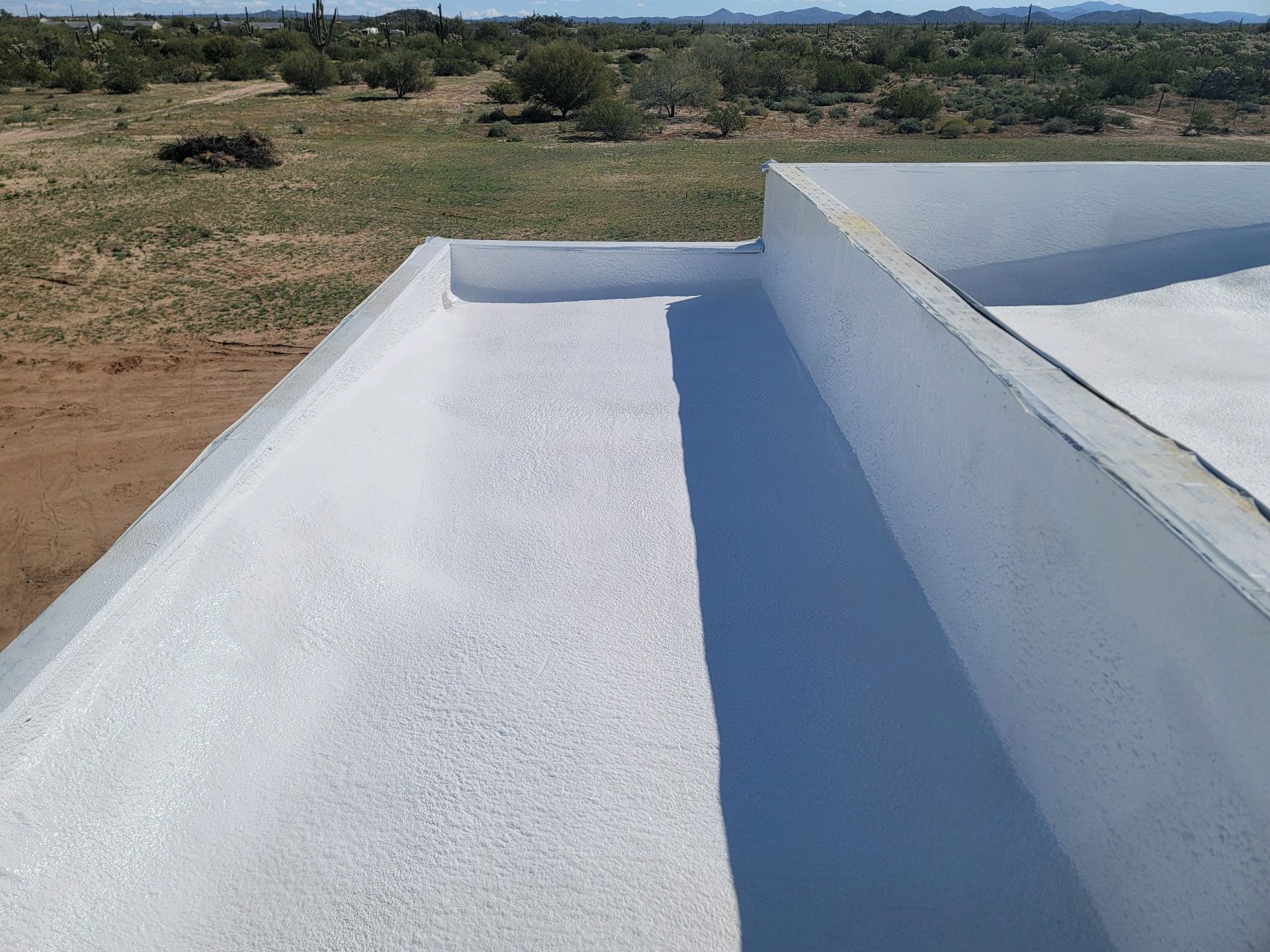 White rooftop with parapet walls overlooking a dry, grassy landscape under a clear sky