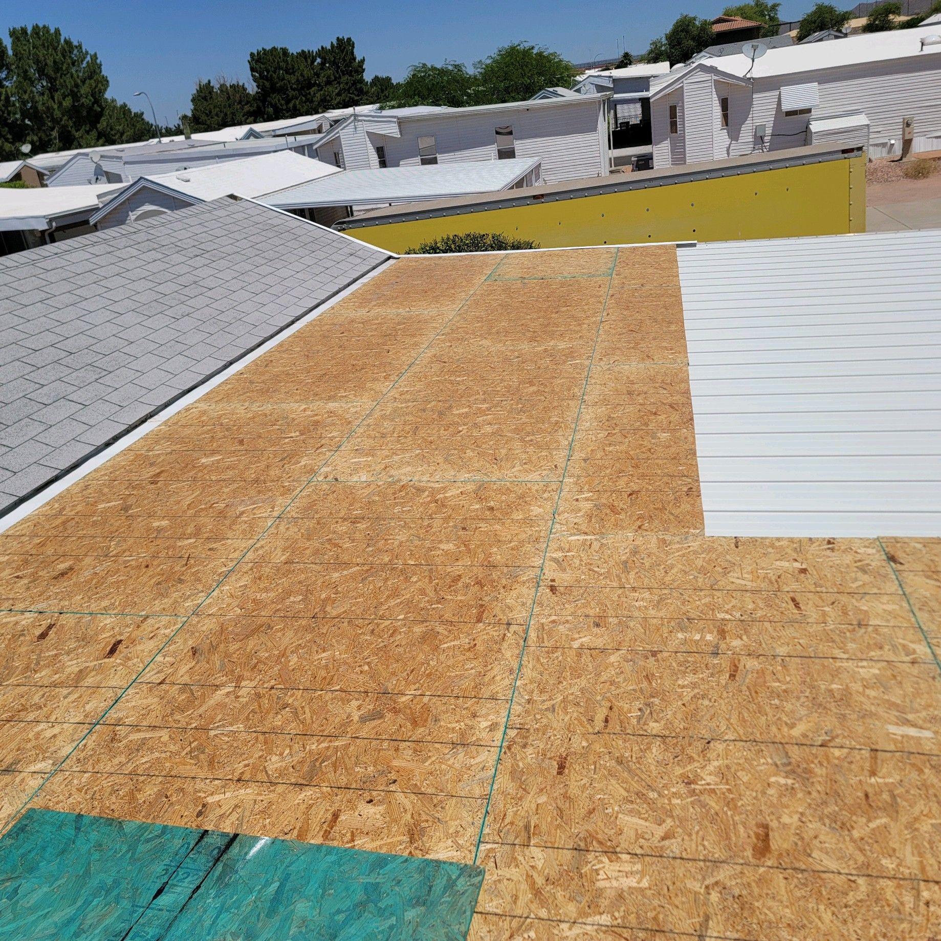 Roof under construction with plywood sheathing and white roofing panels on a sunny day