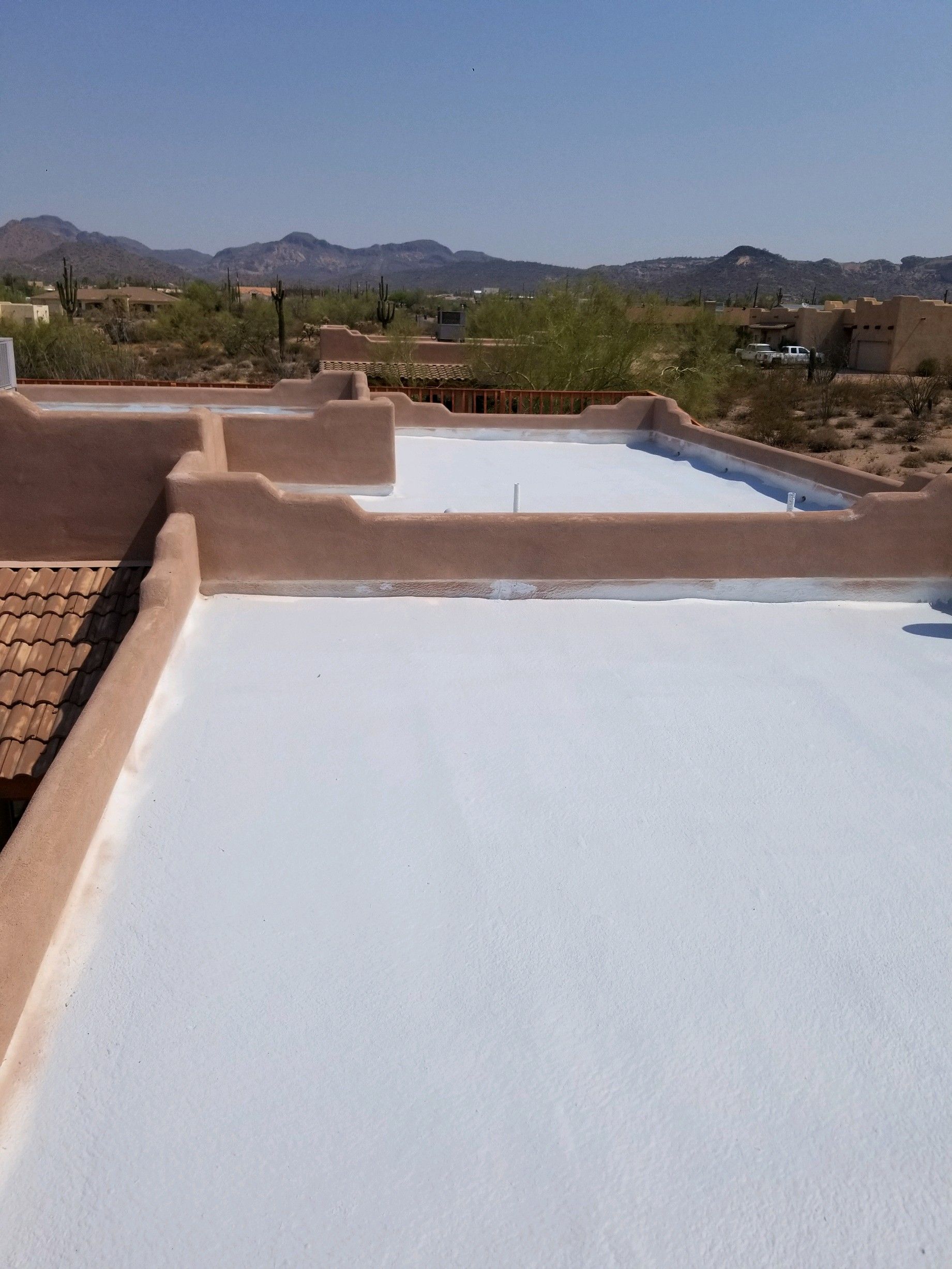 Flat white rooftop with low brick walls, overlooking desert hills and mountains under a clear sky