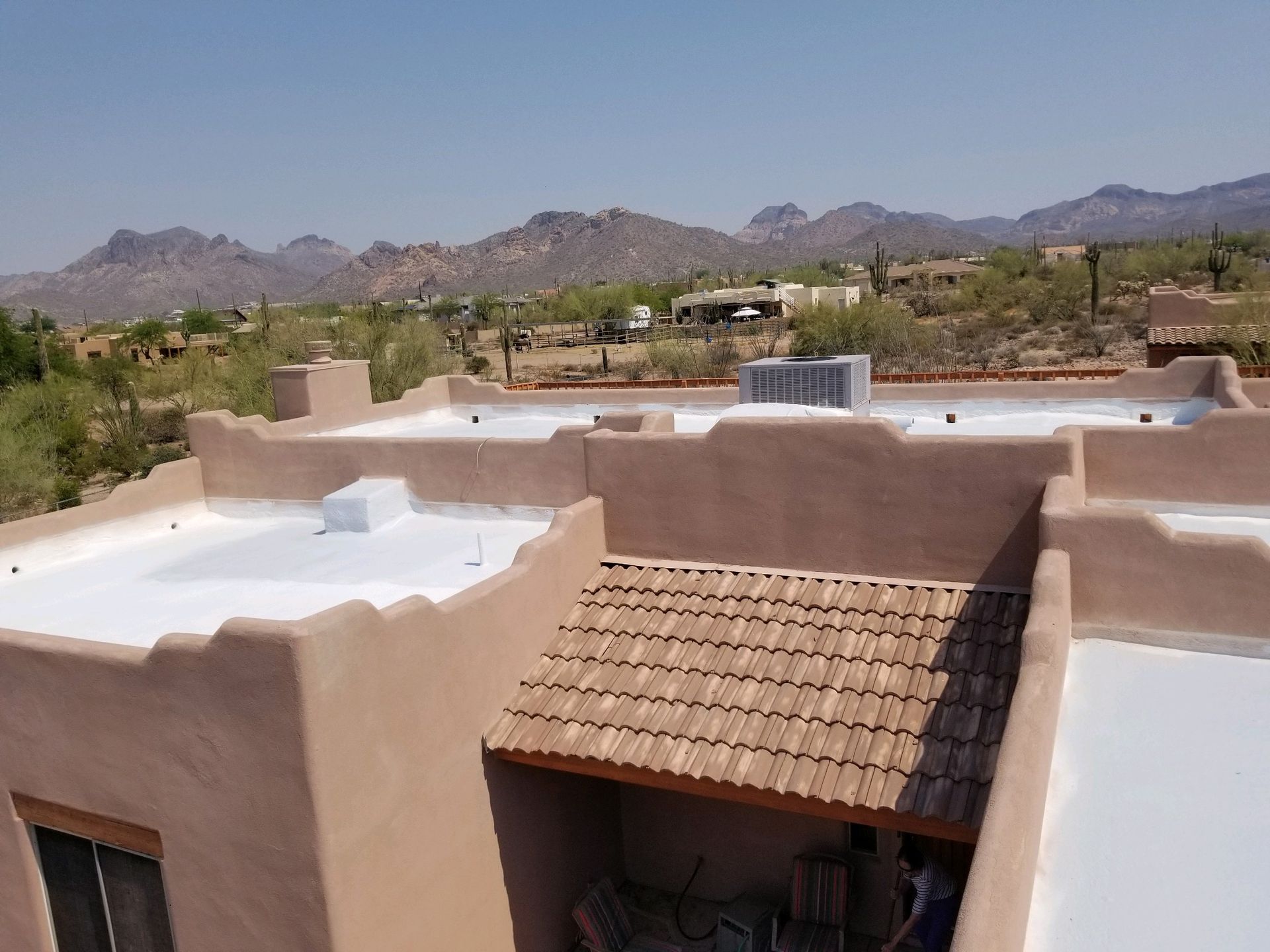 Adobe rooftop with white parapet walls and a tiled awning, overlooking desert mountains.