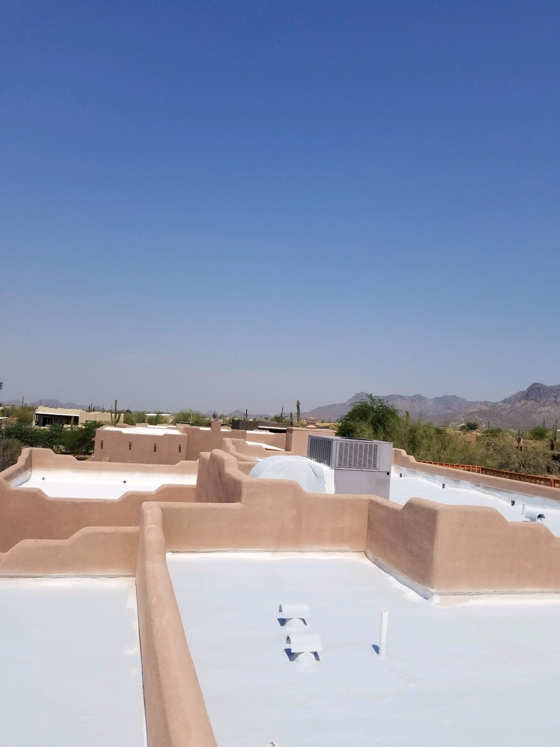 Rooftop view of white and tan buildings under a clear blue sky with mountains in the distance