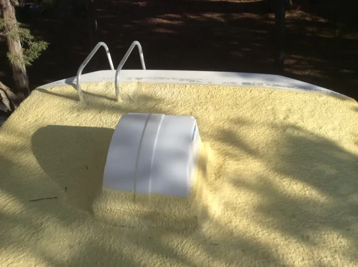 A yellow swimming pool cover with a white floating object and metal ladder by the water.
