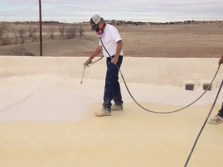 Worker spray-painting a large white surface outdoors on a windy day