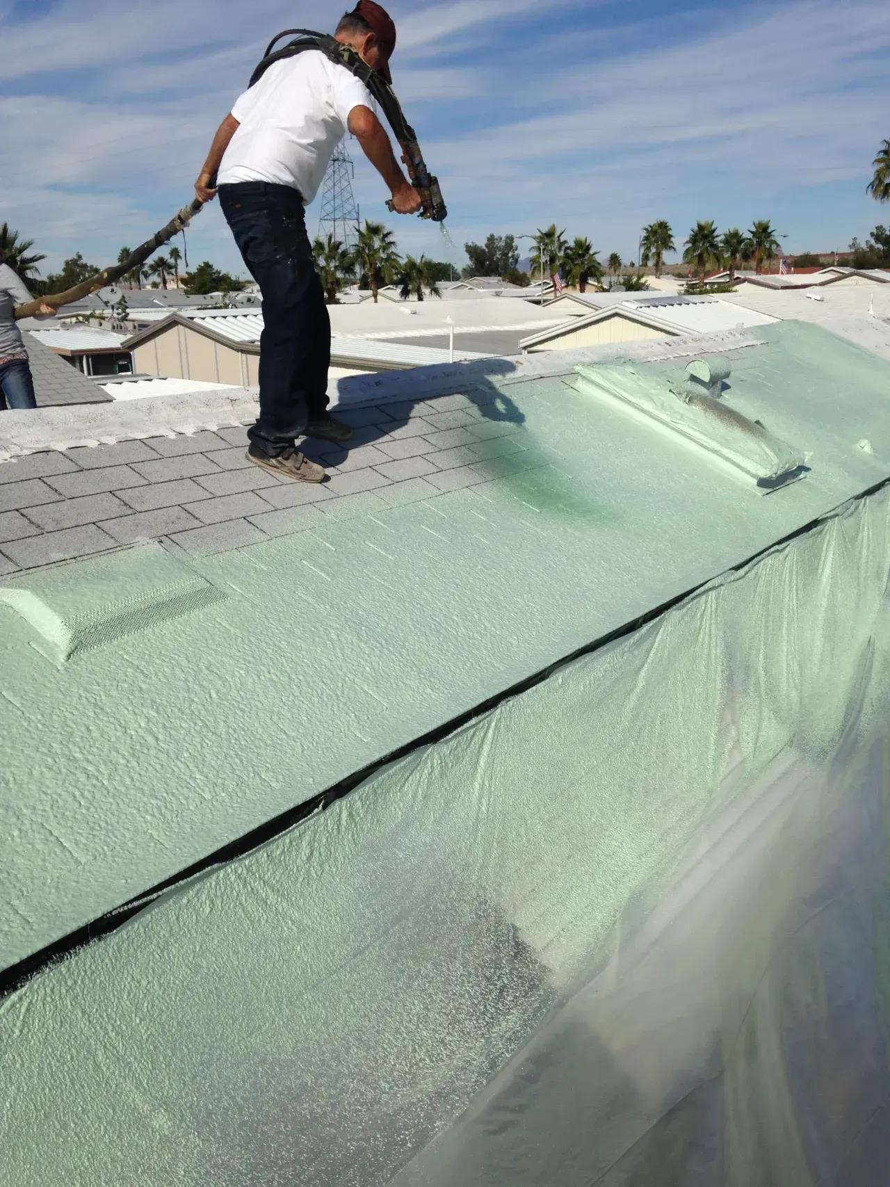 Worker standing on a rooftop applying green spray foam insulation