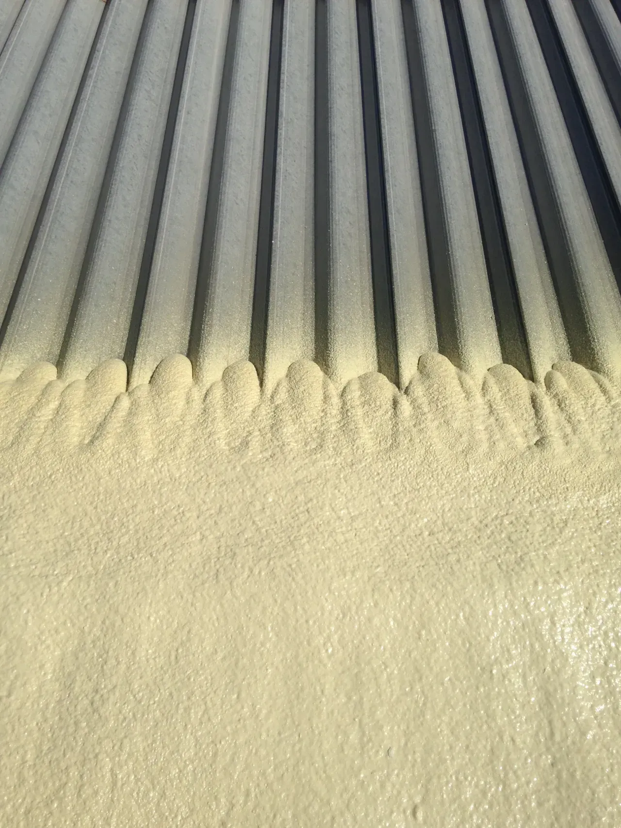 Close-up of gray metal bars coated with pale yellow dust or powder