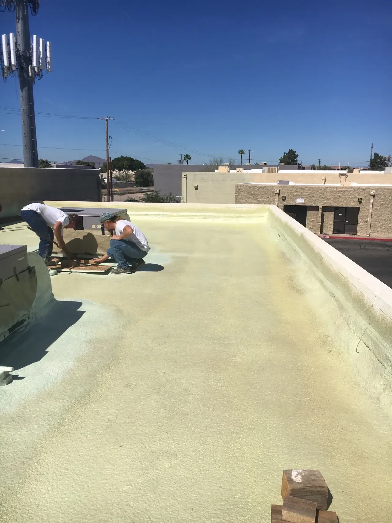 Workers repairing a flat rooftop under a clear blue sky