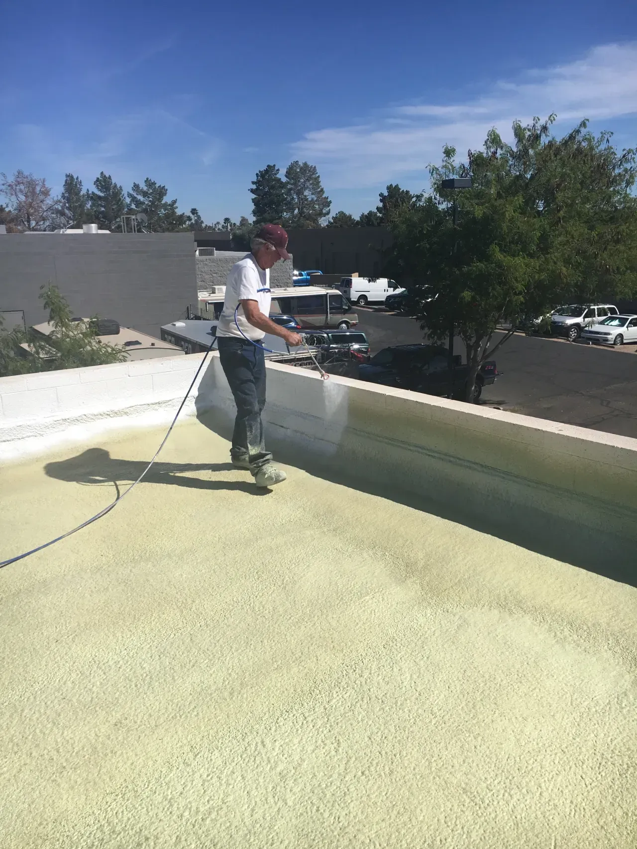 Person pressure-washing a flat rooftop under a sunny blue sky.