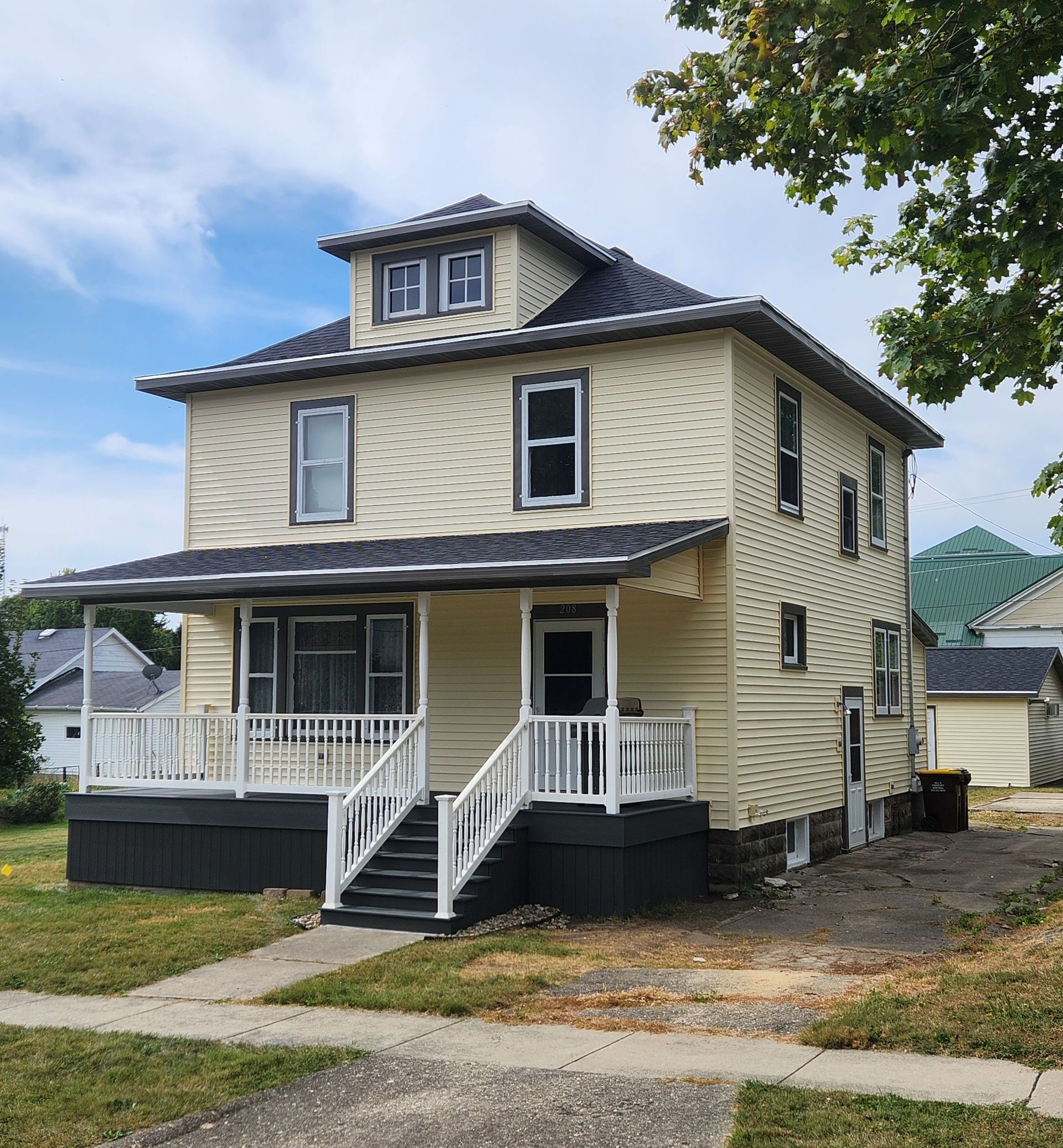 A large yellow house with a black roof and a white porch.