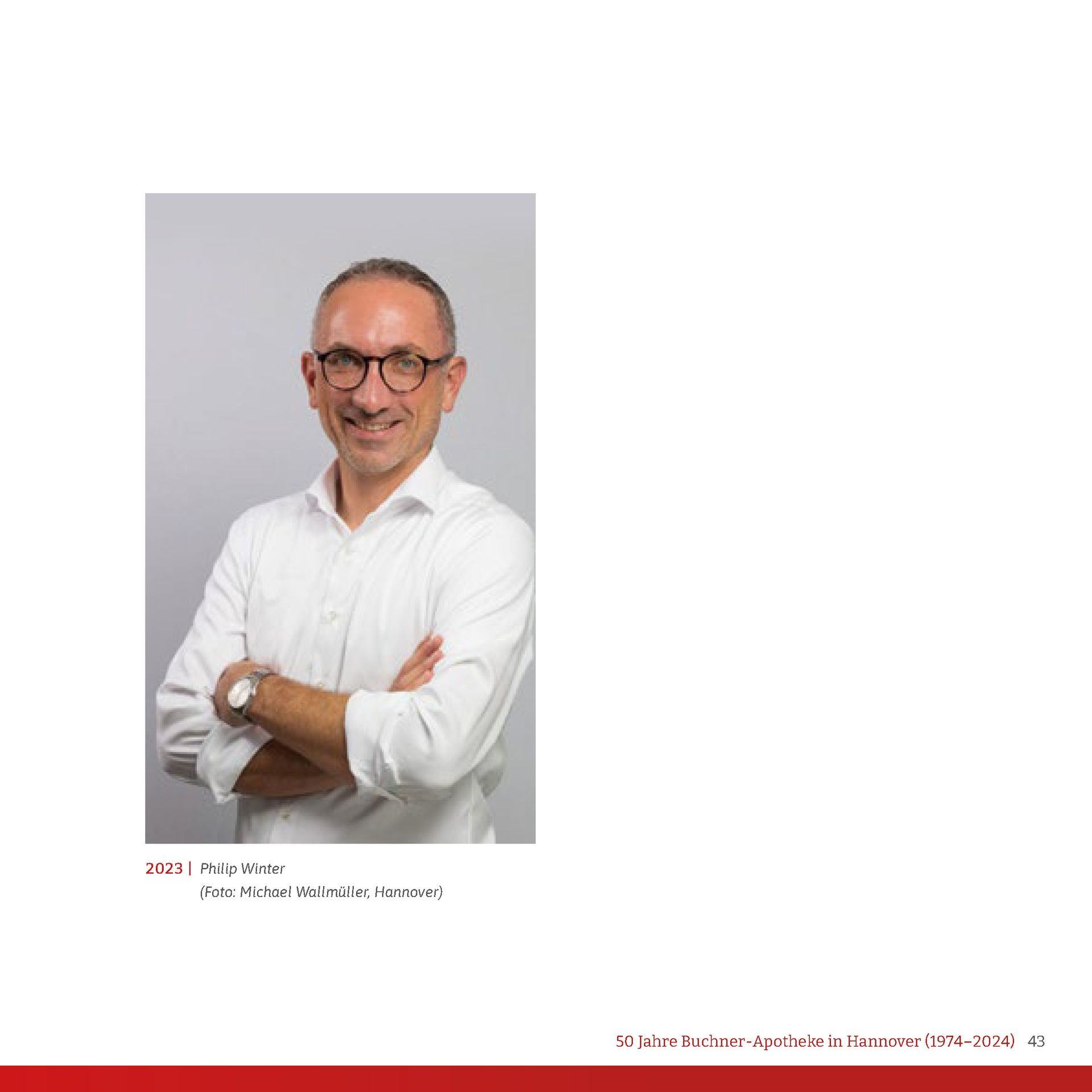 Ein Mann mit Brille und weißem Hemd steht mit verschränkten Armen da.