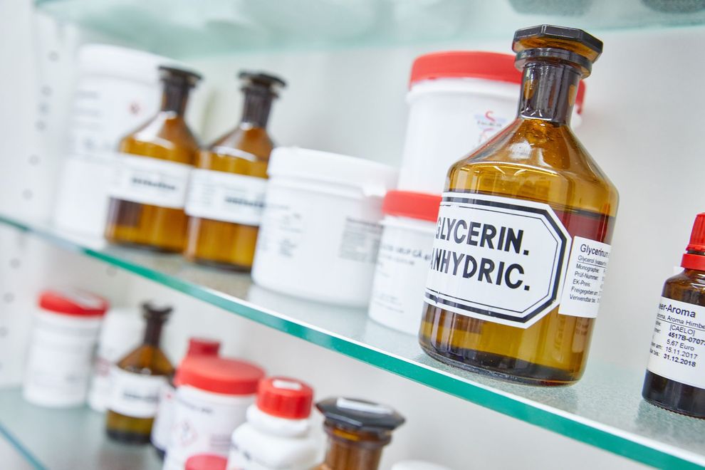 Eine Flasche Glycerin steht neben anderen Flaschen auf einem Glasregal.