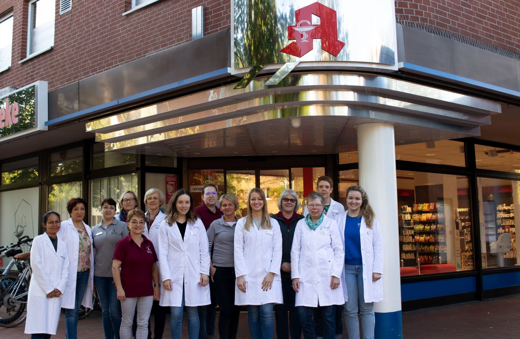 Eine Gruppe von Menschen in weißen Kitteln posiert vor einer Apotheke für ein Foto.
