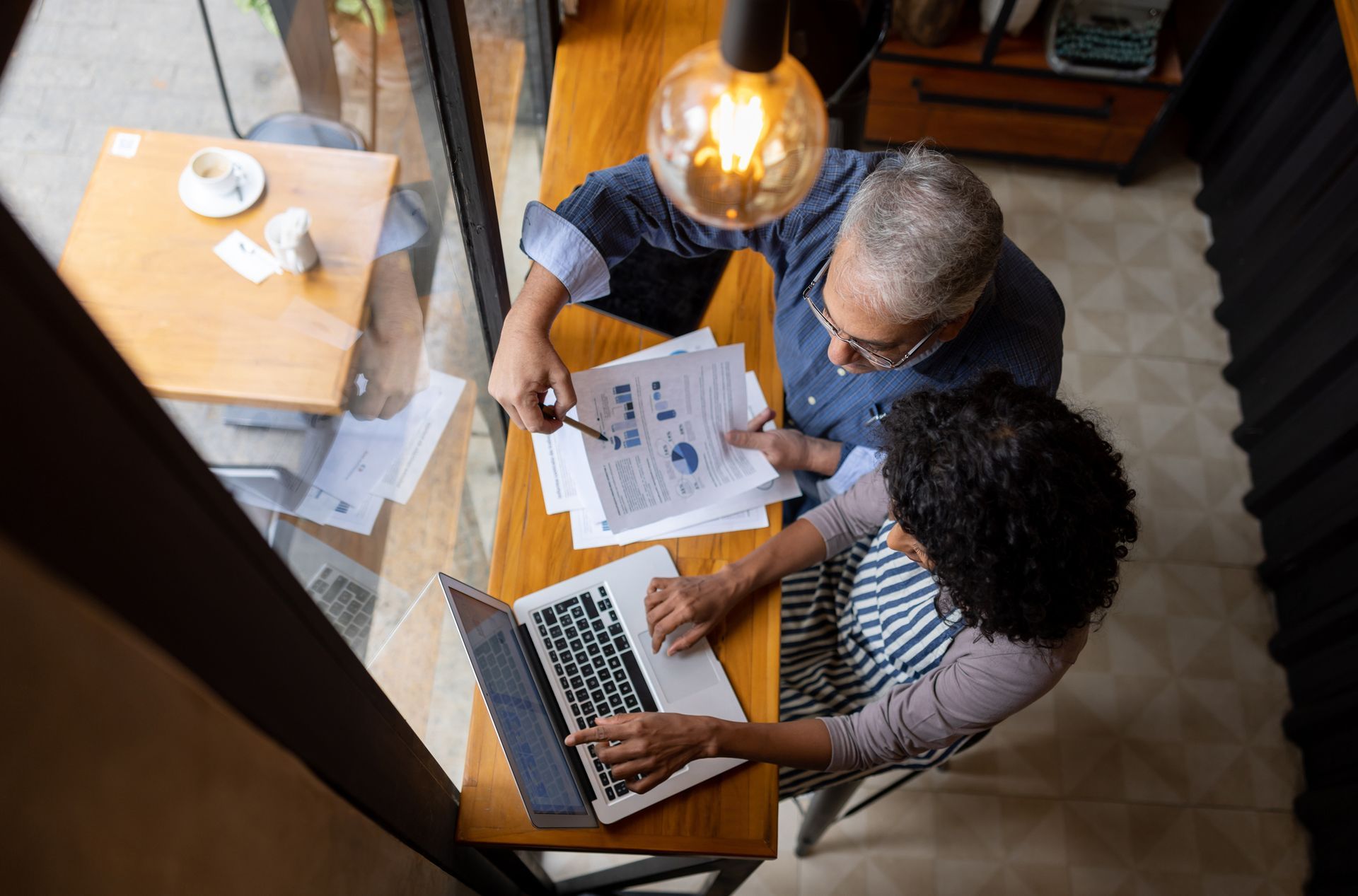 A man and a woman are sitting at a table looking at a laptop.