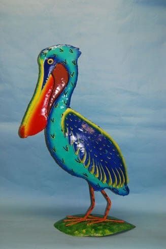 Colorful painted pelican sculpture with a red-orange beak standing on green base against blue background