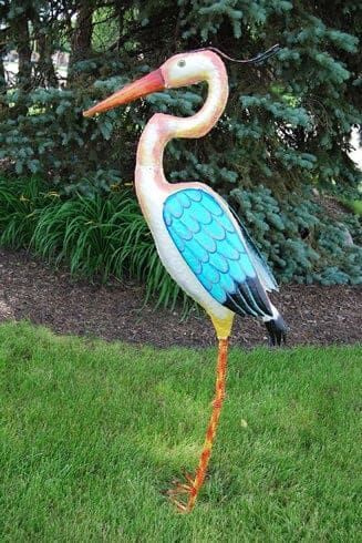 Tall painted stork sculpture with blue wings and orange beak standing on grass outdoors