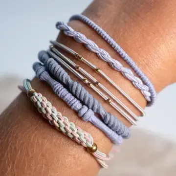 Stacked woven and cord bracelets in lavender, silver, and beige on a wrist