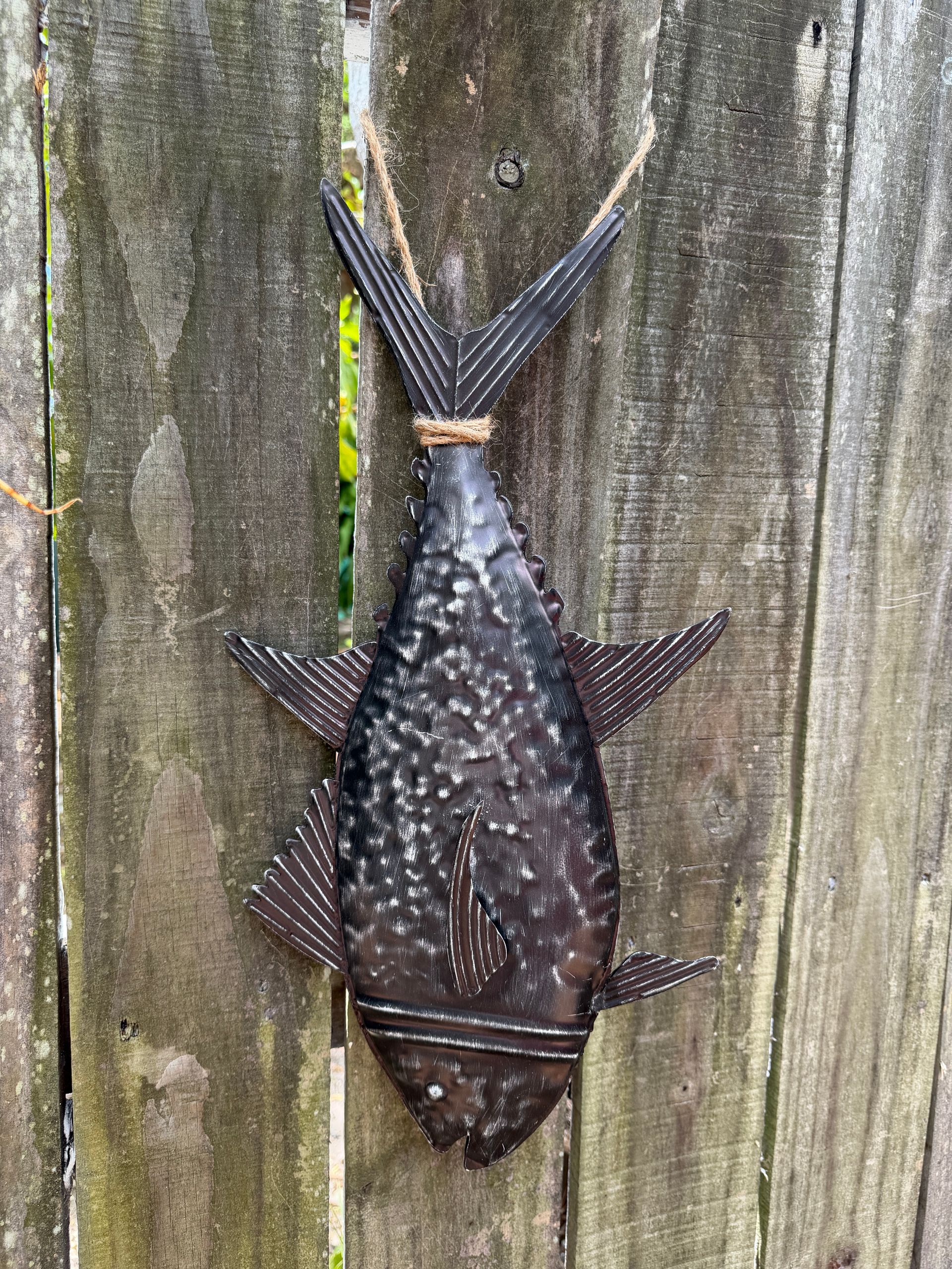 Spotted fish clinging vertically to a weathered wooden fence with tail raised upward