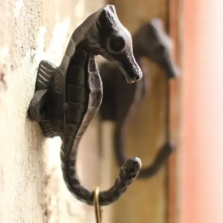 Black seahorse-shaped wall hook on a beige wall with a blurred hook in the background