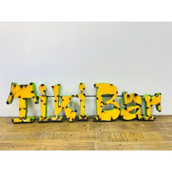 Yellow-and-black decorative letters spelling “Tikibar” on a wooden surface against a white wall