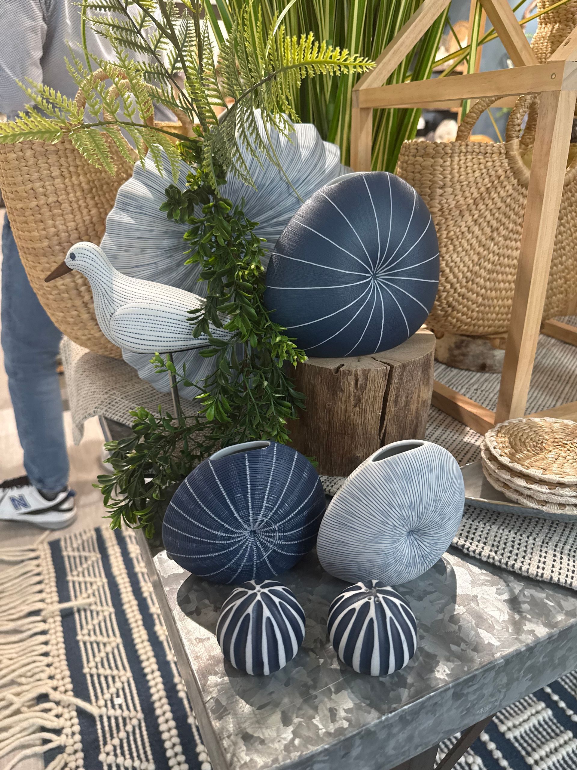 Decorative blue and white painted gourds arranged on a table with greenery outdoors