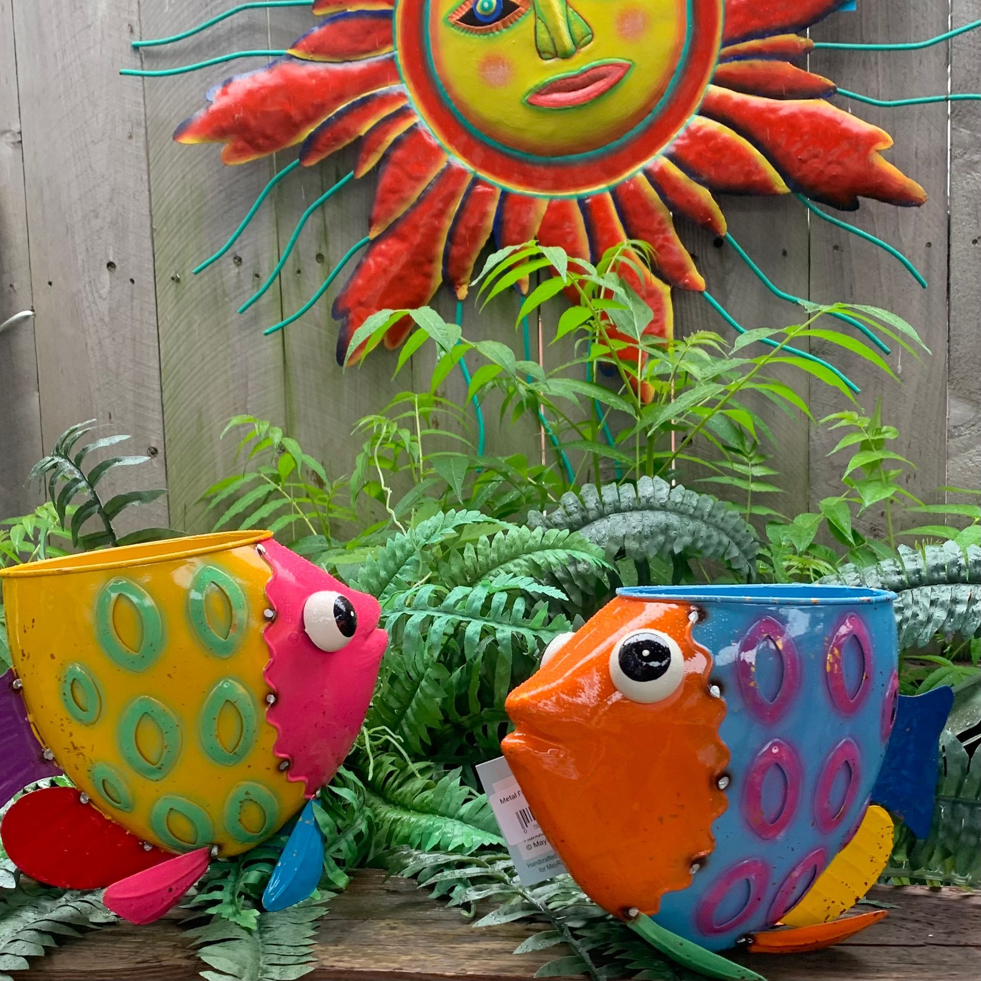 Colorful fish sculptures in a garden beneath a bright sun wall decoration