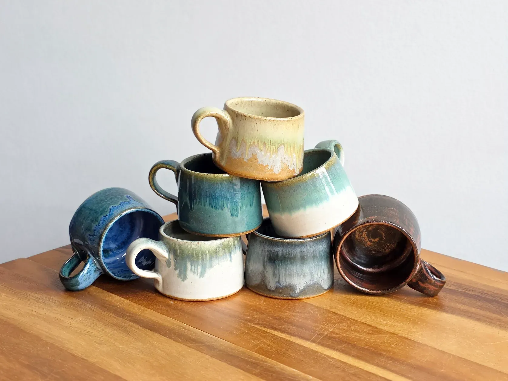 Stack of colorful ceramic mugs on a wooden table.