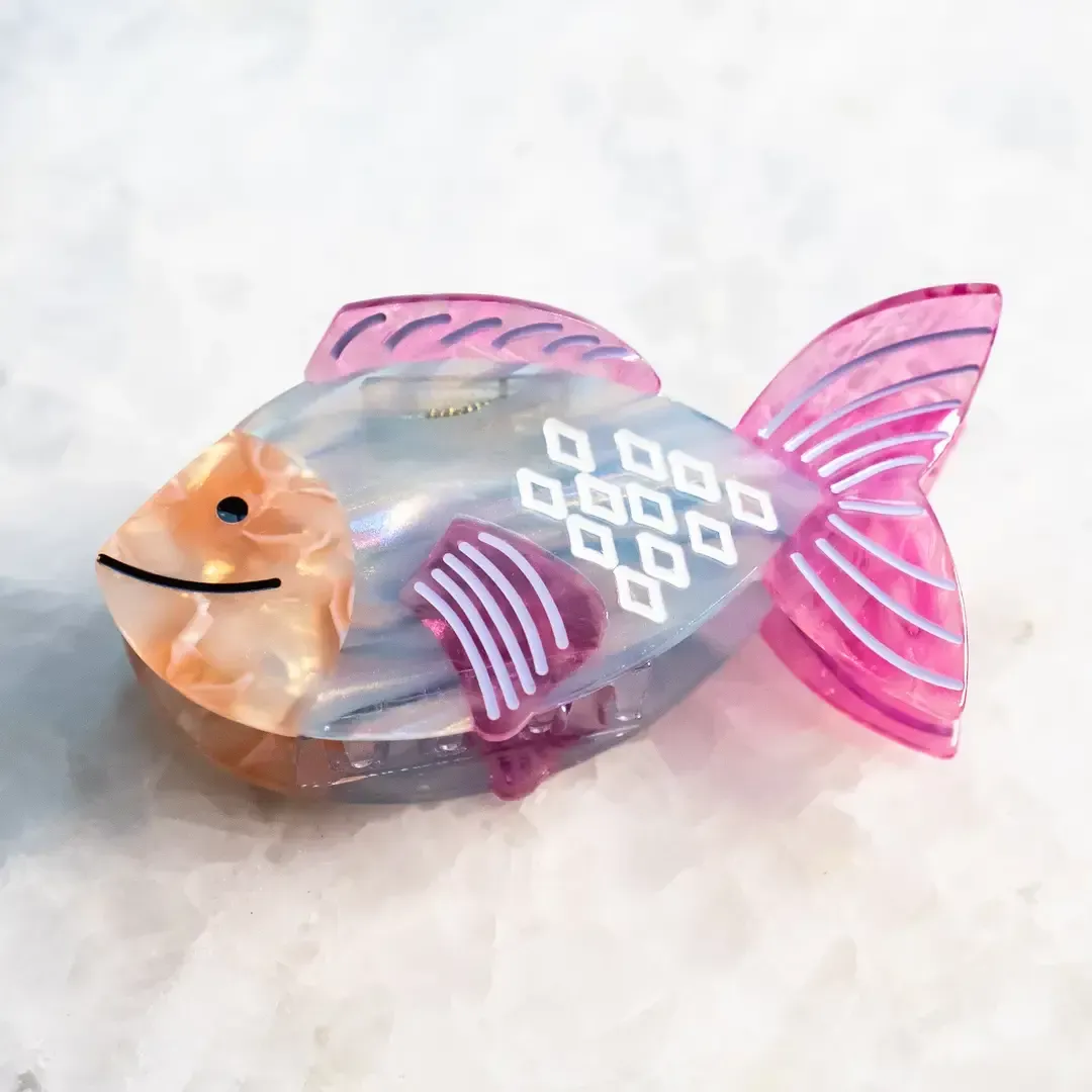 Pink and silver fish-shaped decorative figurine with a smiling face and striped fins on a light background