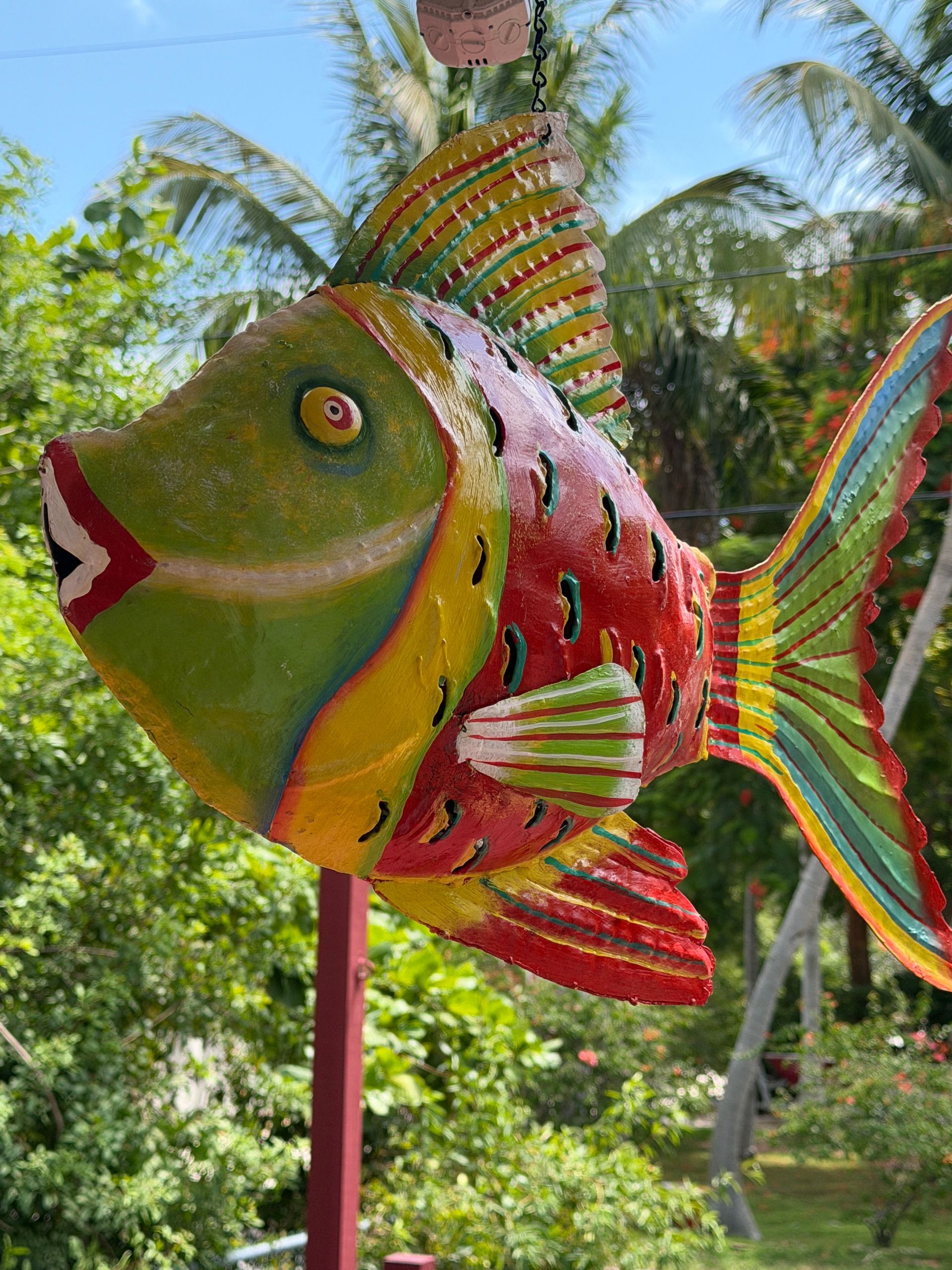 Colorful fish sculpture with red, green, and yellow stripes in a tropical garden
