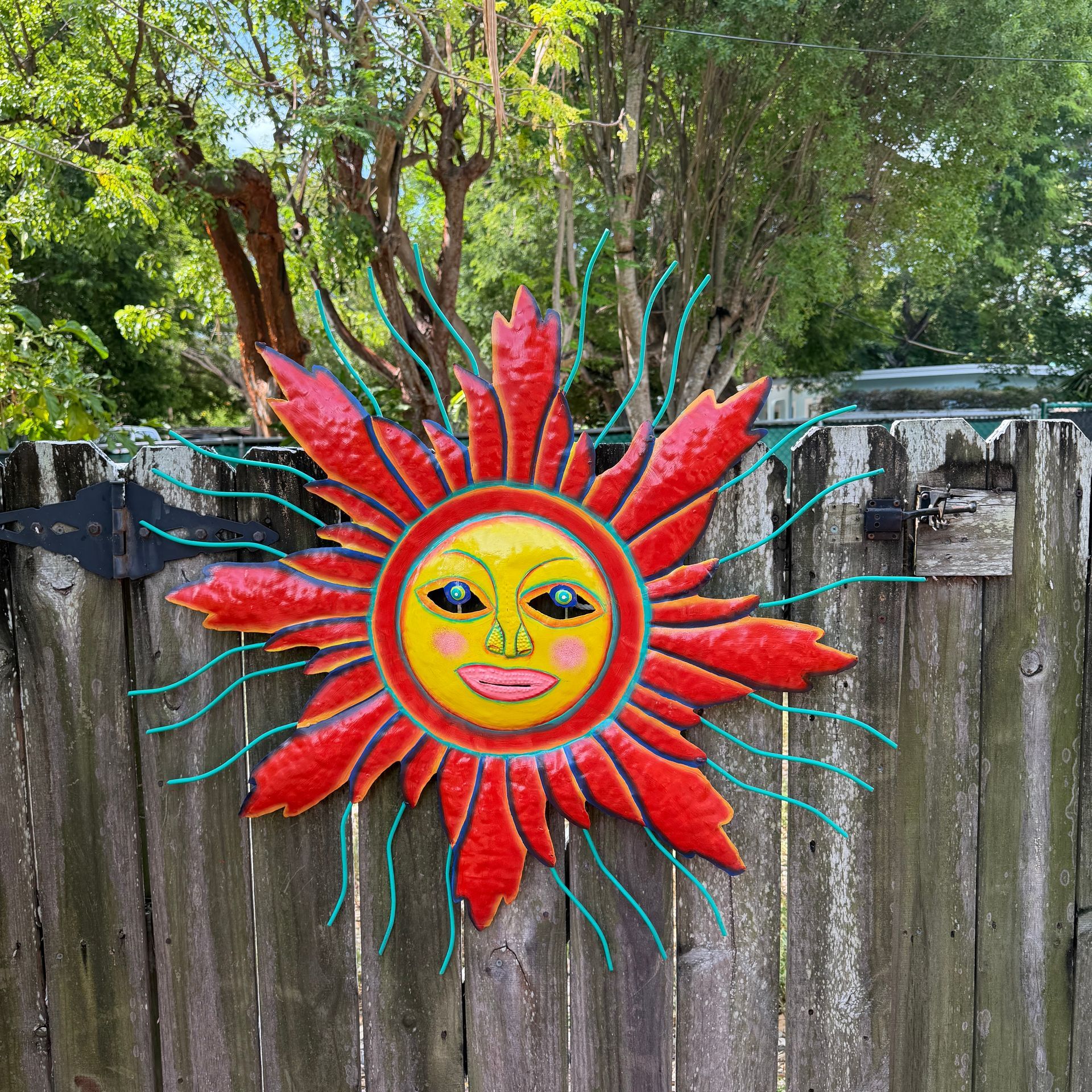 Colorful sun-face wall decoration with red rays on a weathered wooden fence outdoors