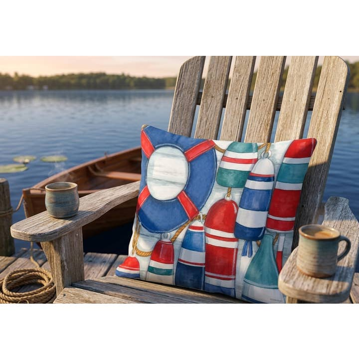 Nautical pillow on a wooden chair by a lakeside dock, with a rowboat and mugs nearby.