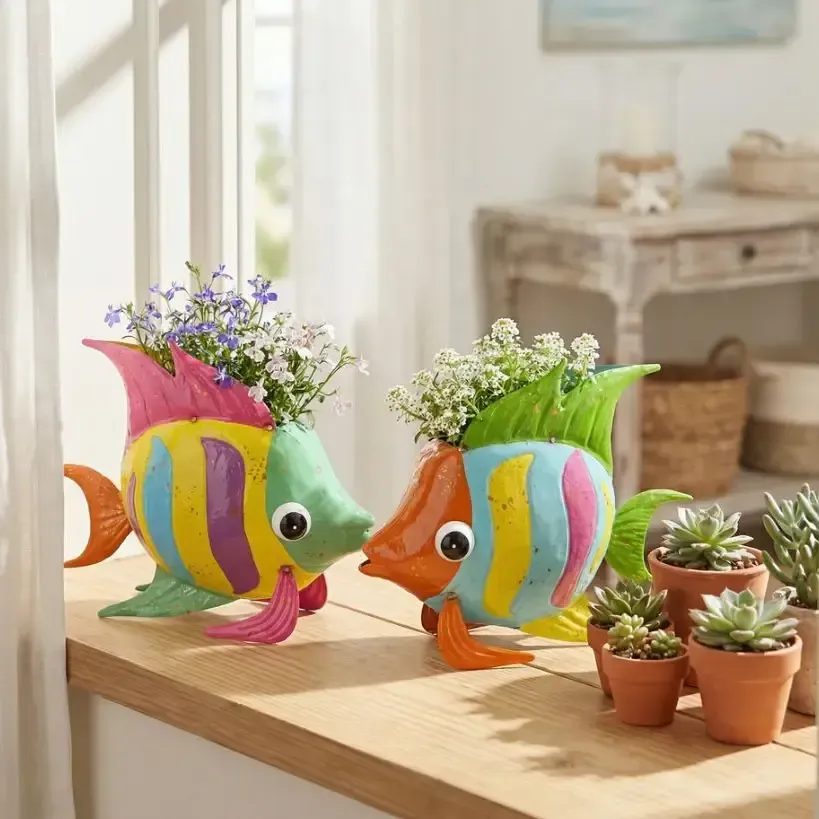 Two colorful fish-shaped planters with flowers on a sunlit wooden table beside small potted succulents