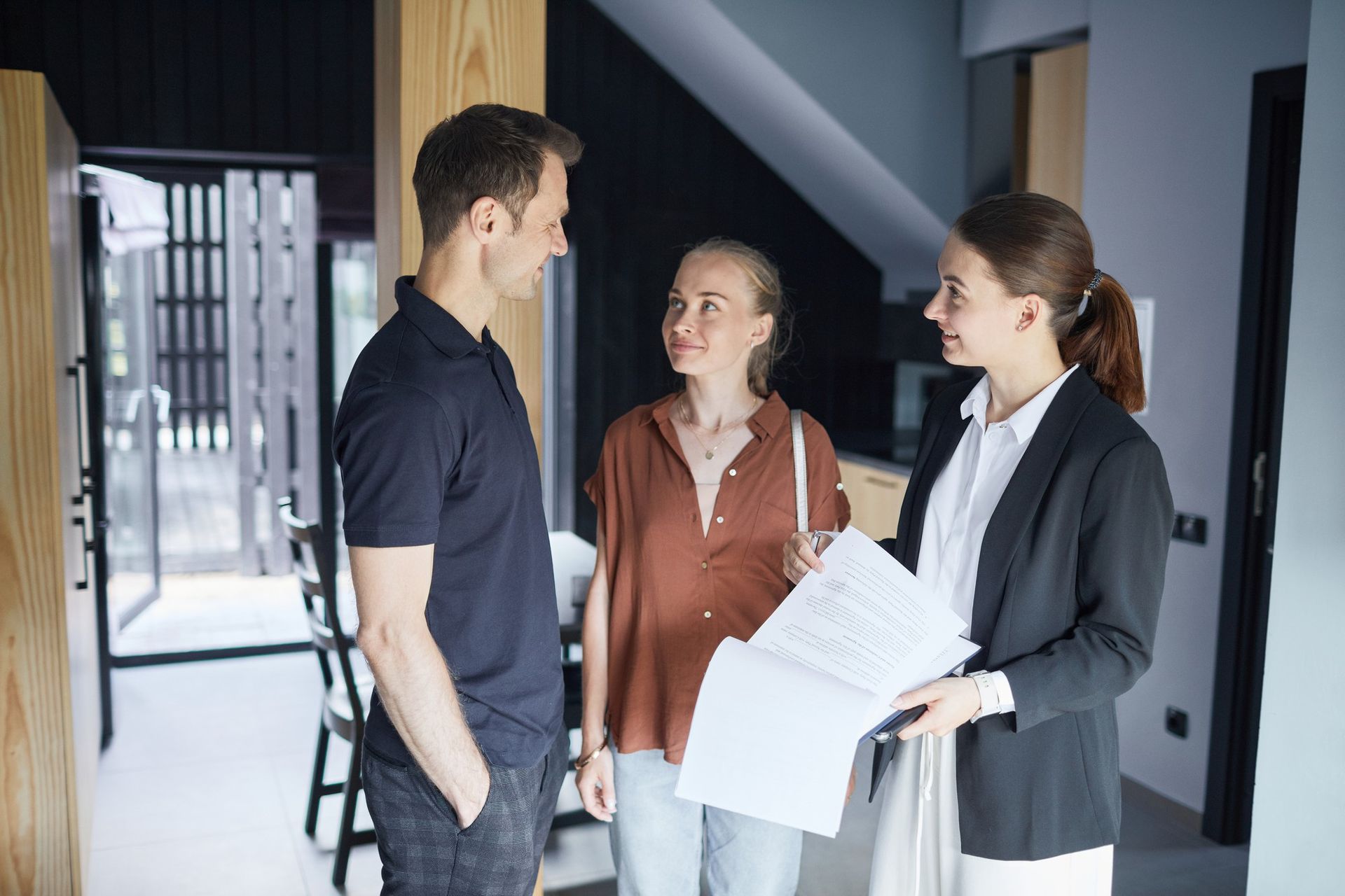 A man and a woman are standing next to each other in a room talking to a real estate agent.