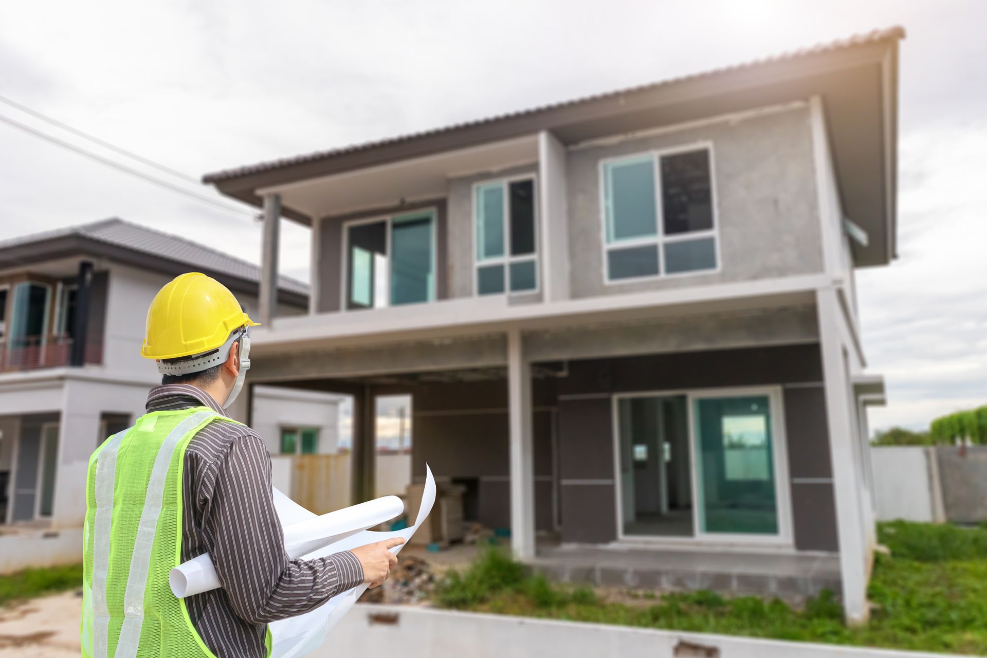A man wearing a hard hat and an orange vest is holding a clipboard in front of a building.