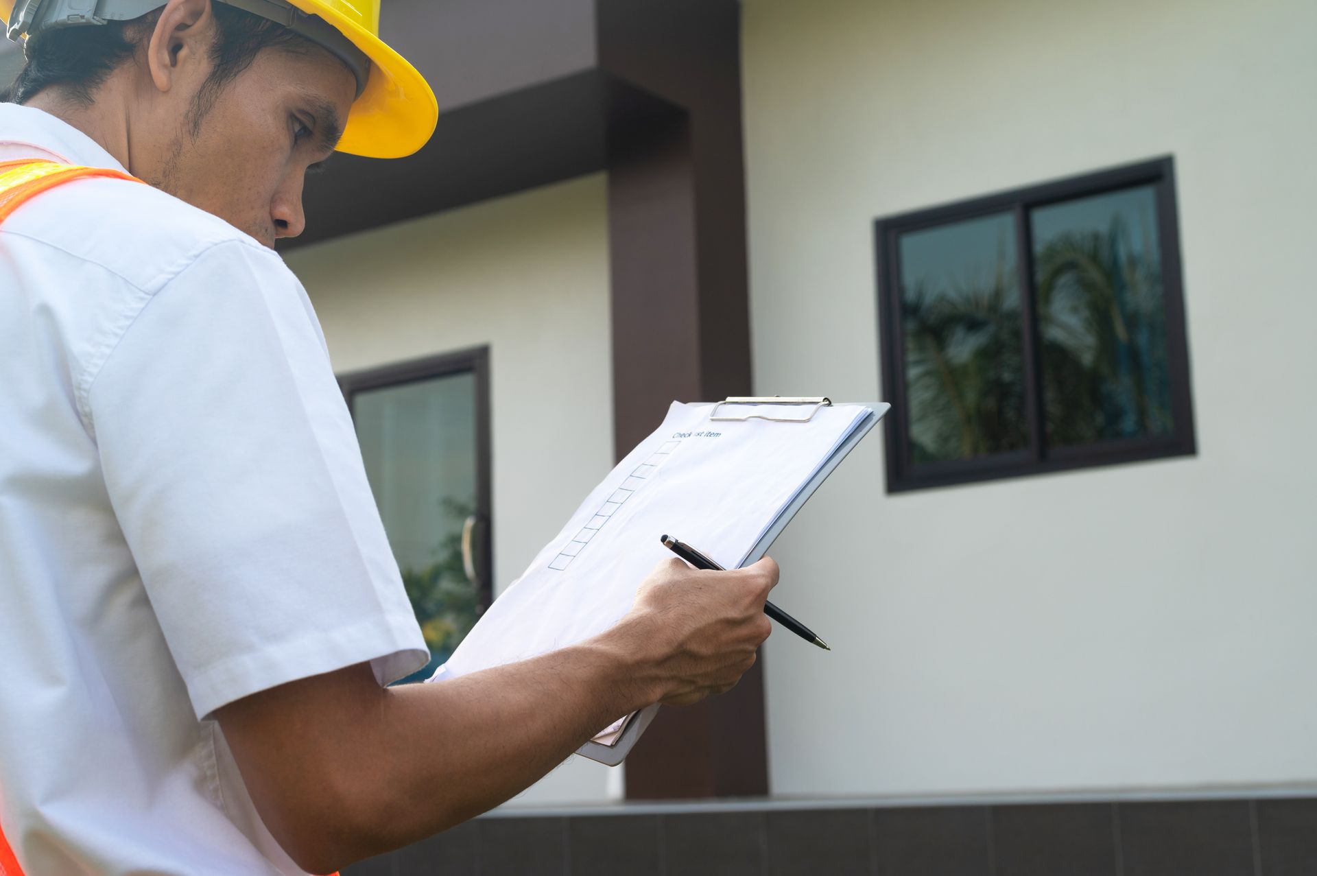 A man wearing a hard hat and safety vest is looking at a clipboard.