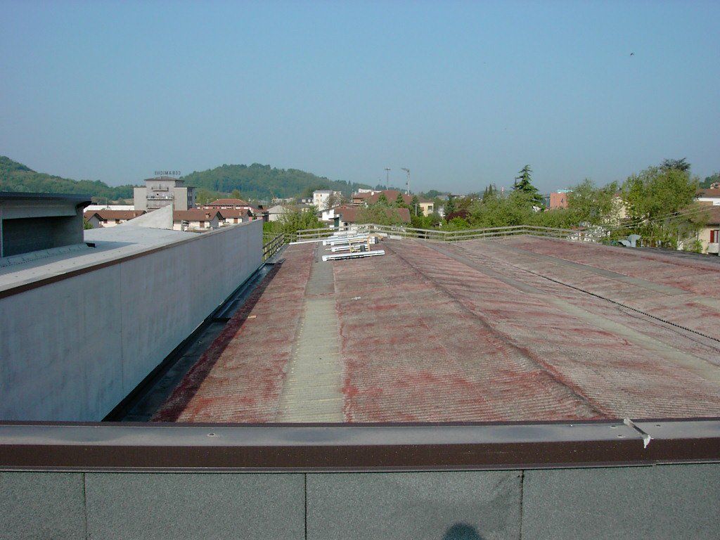 Terrazza sul tetto con muretto basso, tetto rosso e alberi in lontananza sotto un cielo azzurro limpido.
