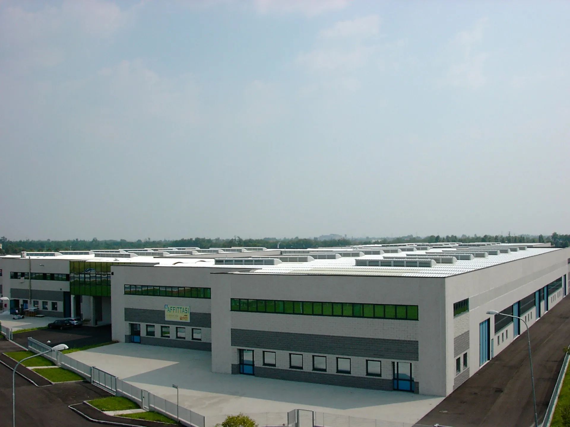 Veduta aerea di un grande magazzino industriale bianco con finestre verdi in un parco commerciale.