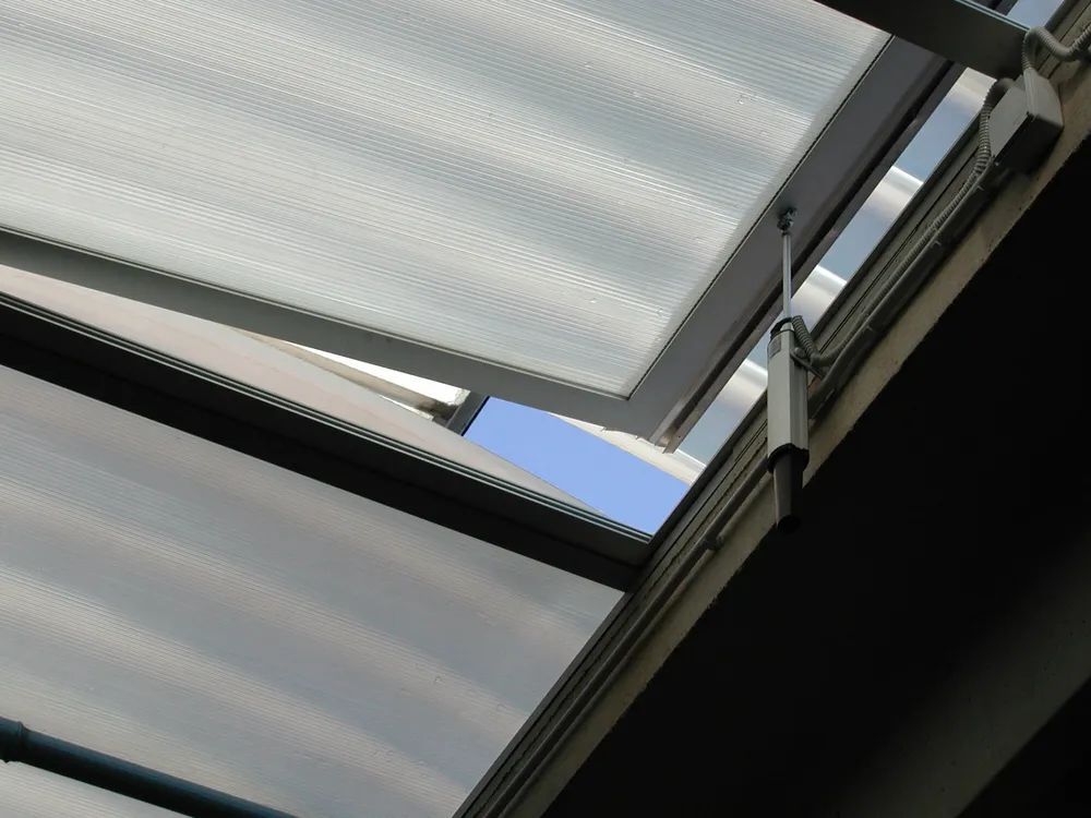 Primo piano di pannelli traslucidi del tetto e travi metalliche scure sullo sfondo di una piccola porzione di cielo azzurro.