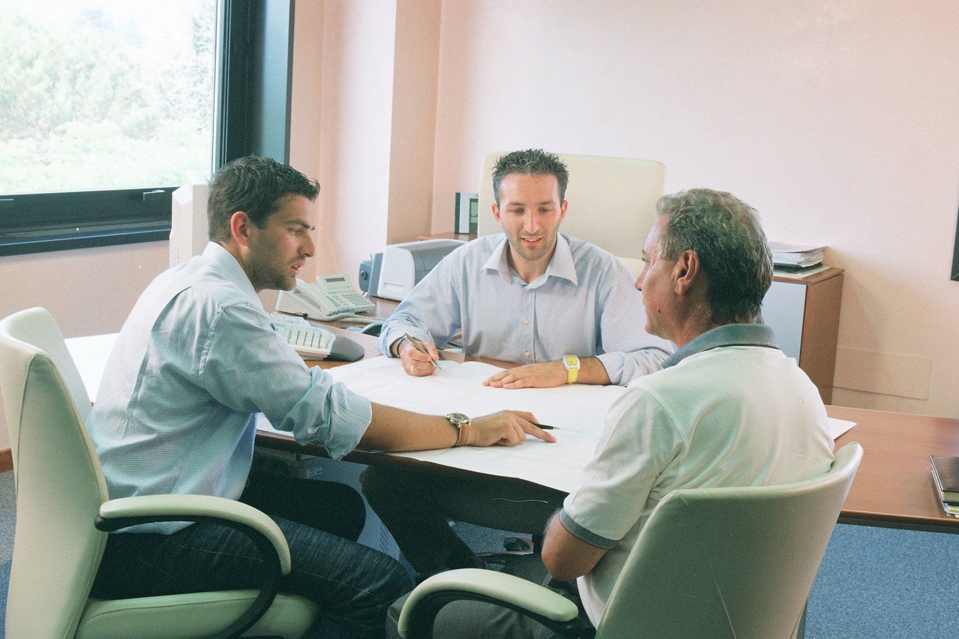 Tre persone riunite attorno a un tavolo in un ufficio luminoso, discutono di documenti.