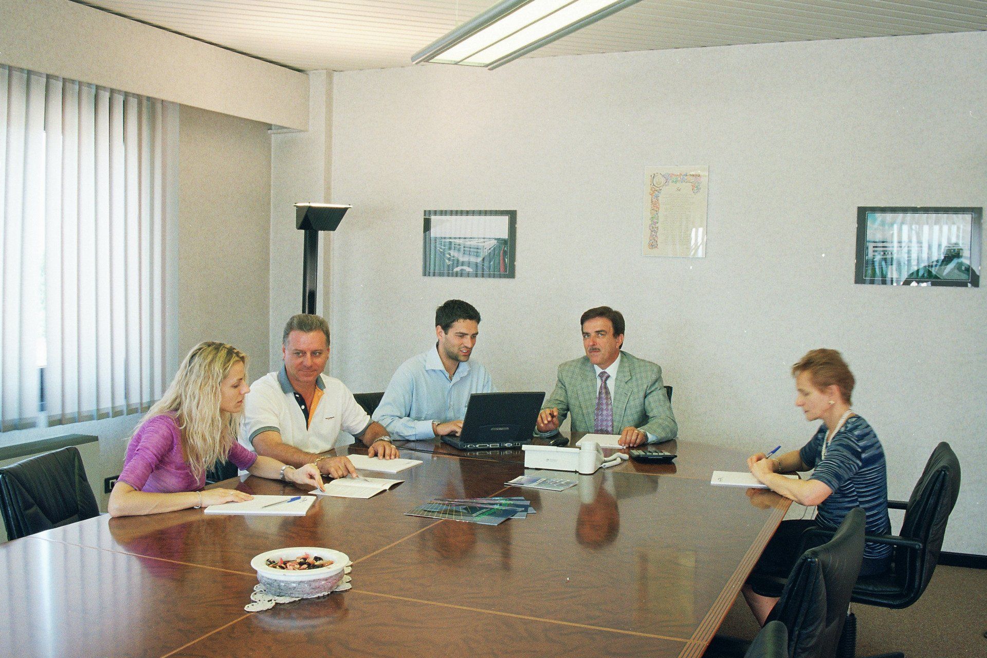 Riunione di gruppo attorno a un tavolo da conferenza in un ufficio luminoso, con un computer portatile e dei documenti.