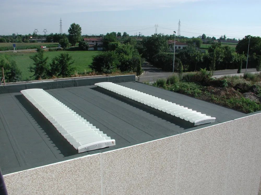 Tetto con due lunghe unità di ventilazione bianche che si stagliano su un paesaggio verdeggiante e sugli alberi sullo sfondo.