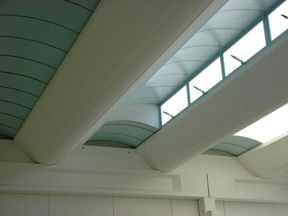 Soffitto con travi bianche e lucernari che lasciano entrare la luce naturale.