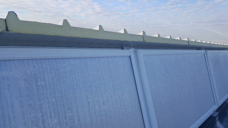 Una recinzione blu per la privacy a lato di una strada sotto un cielo nuvoloso, con un tetto verde visibile sopra di essa
