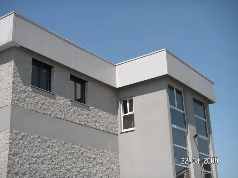 Moderno edificio grigio con tetto e finestre bianche che si stagliano contro un cielo azzurro.