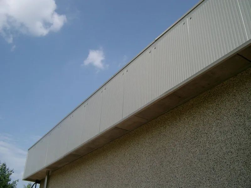 Angolo del tetto di un edificio beige contro un cielo blu con una piccola nuvola.