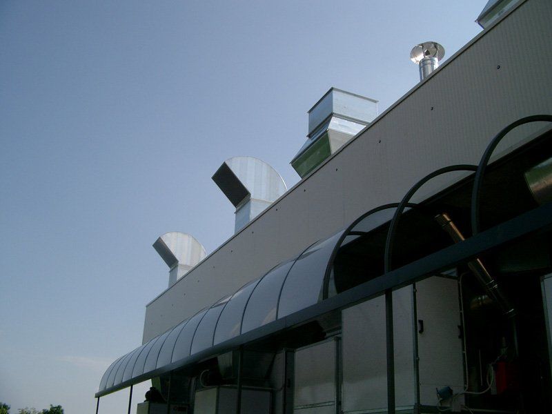 Esterno moderno dell'edificio con tettoia in vetro e prese d'aria sul tetto sotto un cielo limpido