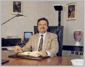 Uomo in abito beige seduto a una scrivania con un libro aperto in un ufficio