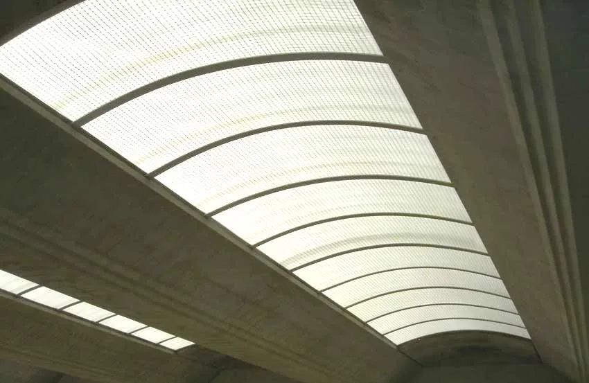 Soffitto con lucernario curvo, pannelli bianchi traslucidi e cornice scura in una struttura interna.