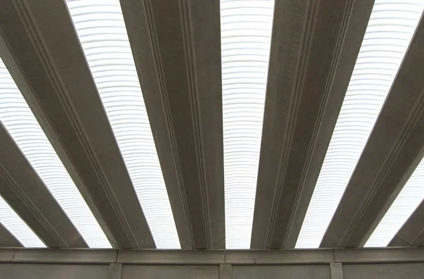 Soffitto con travi scure alternate a lucernari luminosi in un interno in stile industriale.