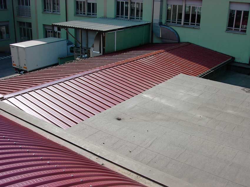 Tetto con sezioni in lamiera ondulata rossa e cemento grigio accanto a pareti verdi dell'edificio