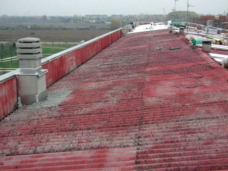 Lungo tetto piatto rosso con prese d'aria e, oltre il parapetto, uno scorcio di paesaggio urbano in lontananza.